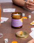 Gros plan sur bougie Fleur de Saule en verre ambré avec flamme vive et couvercle doré brossé sur table en bois