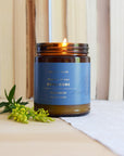 Gros plan sur bougie Cardamome en verre ambré avec flamme lumineuse et étiquette bleu-gris de Baltic Club