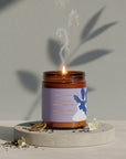 Close-up of Earl Grey Tea soy candle with amber glass, lavender label, and delicate smoke curls