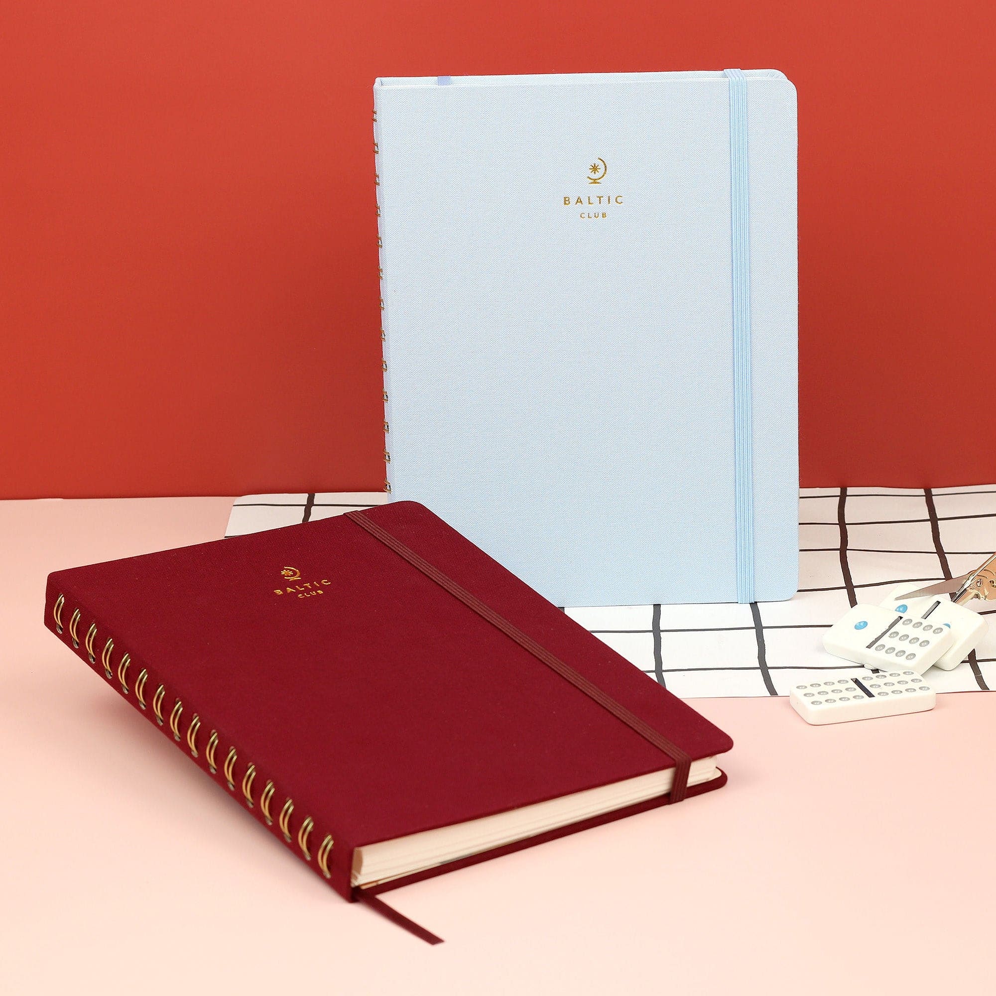 The Blue Ash Cloth-covered Undated Planner on a table next to a burgundy-covered one