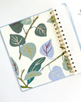 Agenda à spirale ouvert avec motifs botaniques vert sauge et bleu pastel, accents dorés