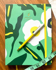 Vue de dessus de l’Agenda non daté Murmure à couverture florale verte vibrante et élastique jaune, accompagné d’un stylo jaune brillant