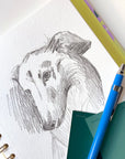 Gros plan du carnet à dessins Murmure avec croquis au crayon de chien sur papier blanc texturé et spirale laiton