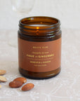 Close-up of Honey Fig & Ginger soy candle in amber glass with golden label and scattered almonds