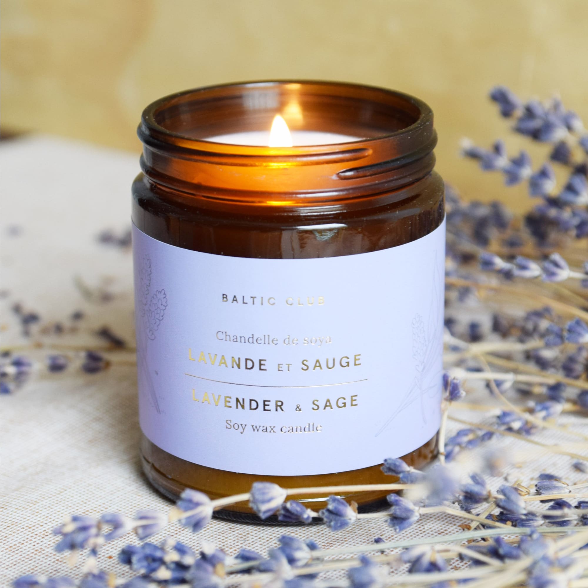 The Baltic Club's Lavender & Sage Soy Candle lit and featured with lavender branches
