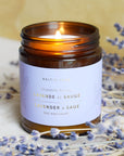 The Baltic Club's Lavender & Sage Soy Candle lit and featured with lavender branches