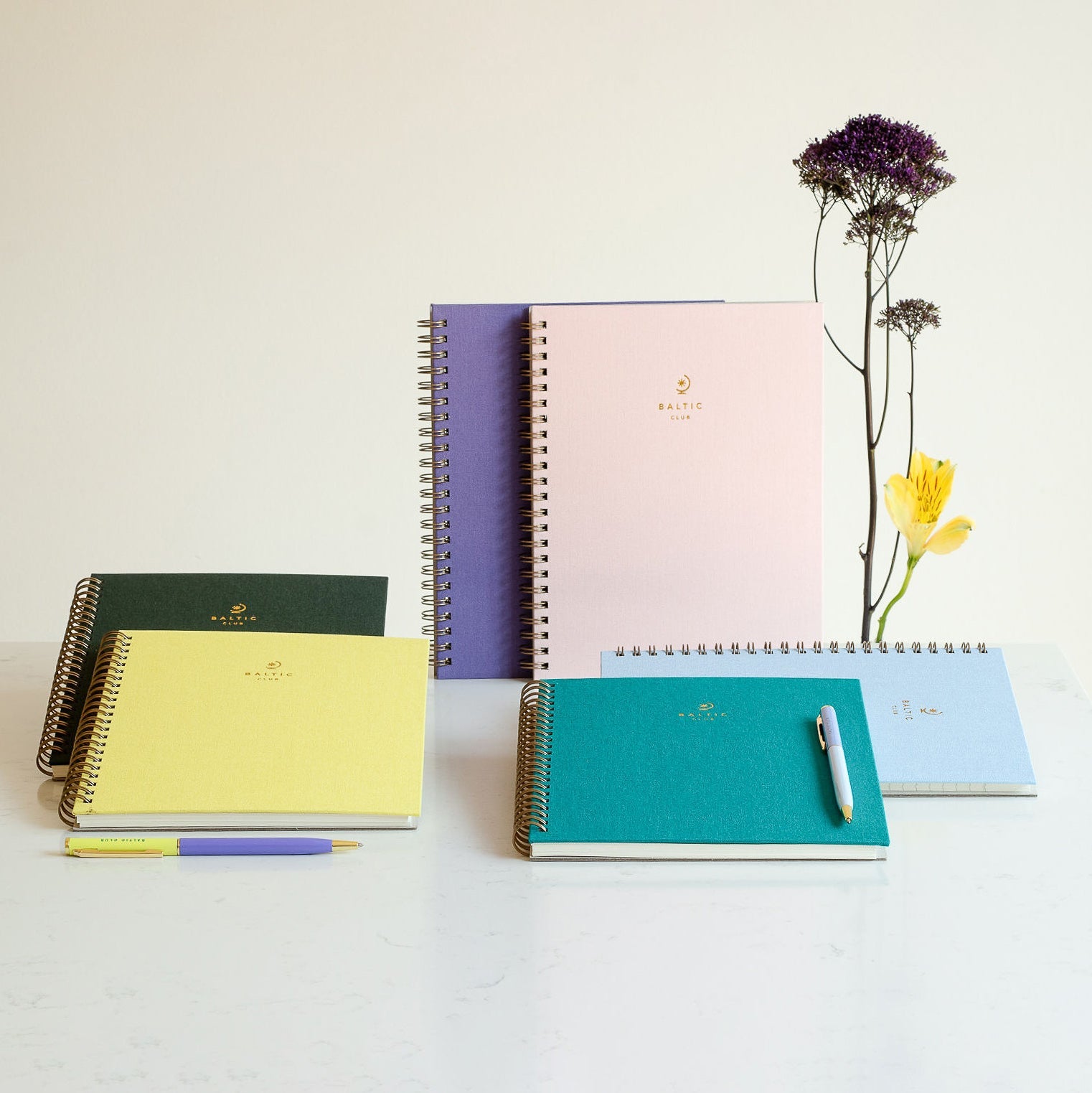 Collection de carnets spirales aux couleurs pastel avec stylos assortis sur surface en marbre clair et fleurs