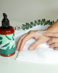 Person applying Baltic Club moisturizing lotion on hand with eucalyptus leaves and white towel on marble surface