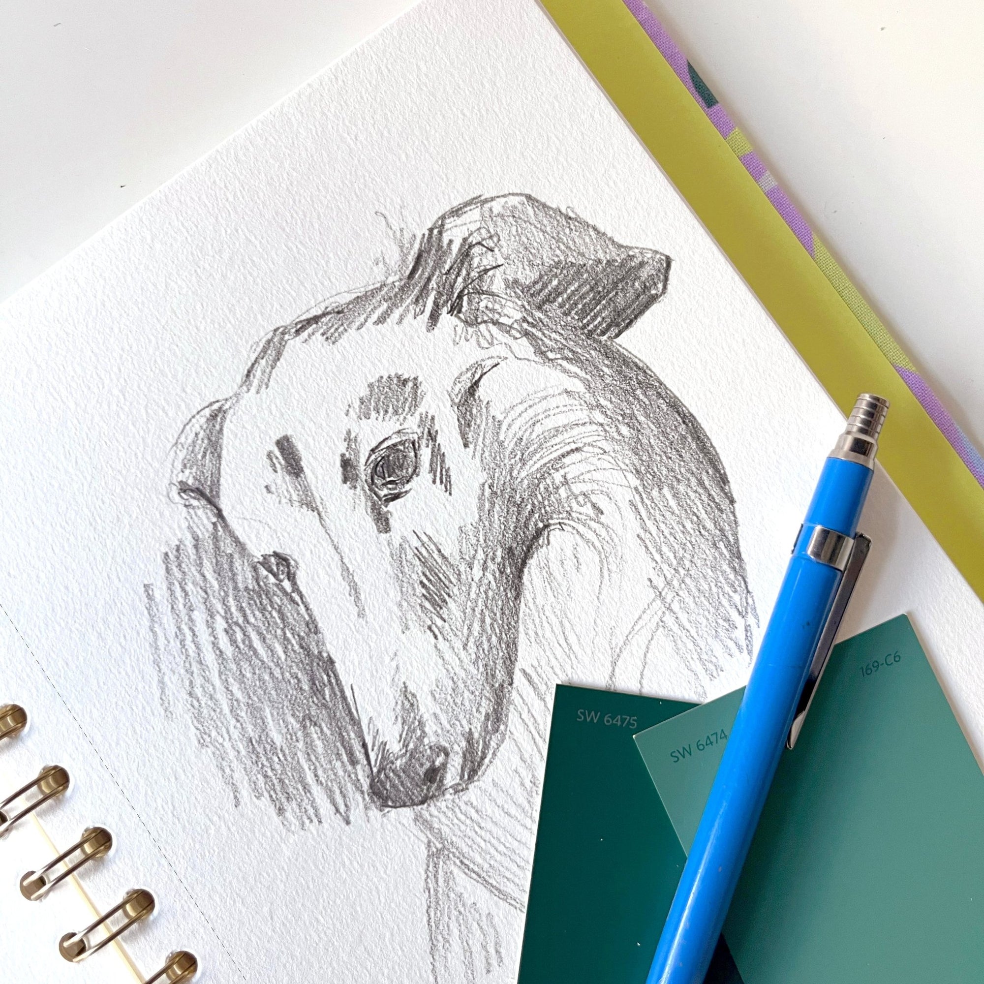 Gros plan du carnet à dessins Murmure avec croquis au crayon de chien sur papier blanc texturé et spirale laiton